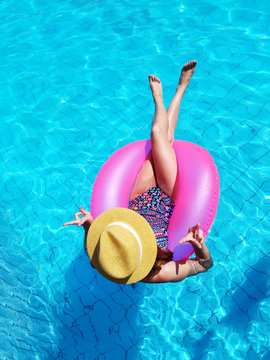 Young beautiful girl relaxing and swimming in the blue swimming pool with a pink circle closeup