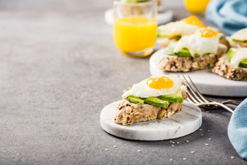 Healthy breakfast with open sandwich with fresh avocado and fried quail egg on small marble board on gray background. Copy space.