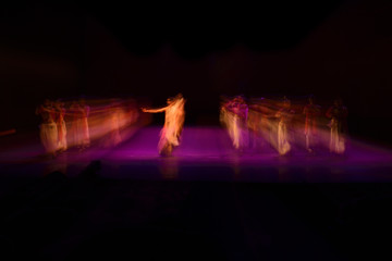 A group of people dancing on stage against black background. 