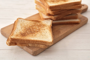Wooden board with tasty toasted bread on table