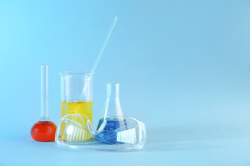 Chemical glassware with colorful samples and lab goggles on color background