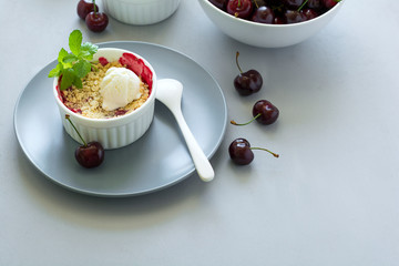 Cherry crumble with oatmeal and ice cream in bowl on grey wooden desk. Summer healthy food