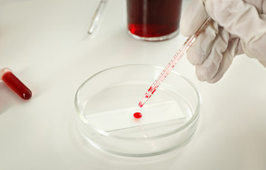 Lab worker dripping blood in petri dish on table