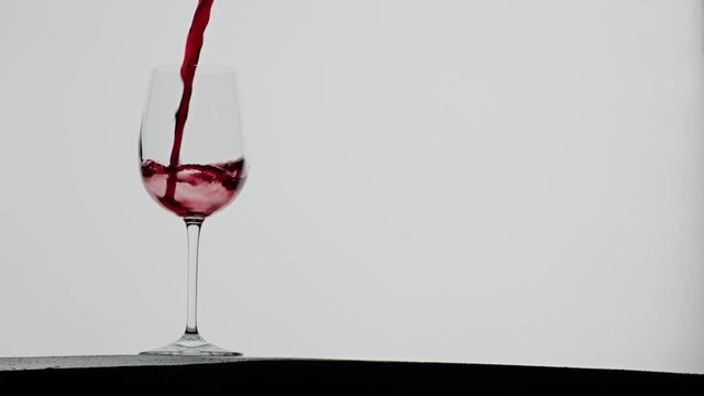 Red vine poured into a vine glass, dramatic slow motion splash