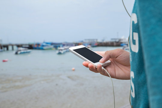 Close up hand using mobile phone. Detail of man hand holding smartphone while listening to music with earphone on the bridge at the pier