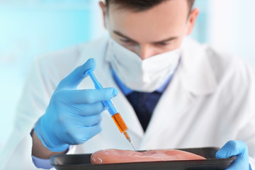 Scientist with syringe examining meat sample in laboratory