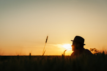 Young man resting in the wheat field at the sunset