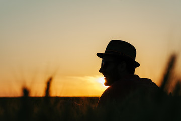 Young man resting in the wheat field at the sunset