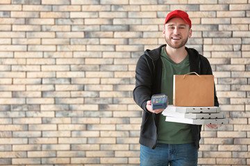 Young man with cardboard pizza boxes, paper bag and bank terminal on brick wall background. Food delivery service