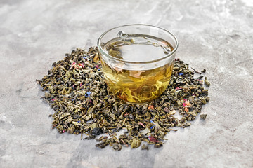 Glass cup of aromatic green tea and dry leaves on grey background