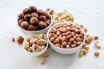 Bowls with different kinds of nuts on light background