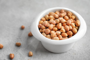 Bowl with peanuts on grey background