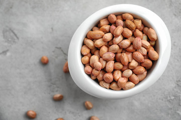 Bowl with peanuts on grey background, top view