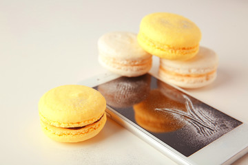Tasty macarons with phone on white background