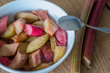White bowl with stewed rhubarb and small spoon on wooden background. close-up.