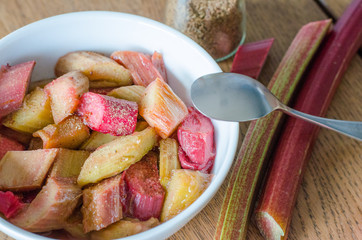 White bowl with stewed rhubarb and small spoon on wooden background. close-up.