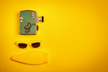 yellow holiday background with an old camera, swimming goggles and sunscreen