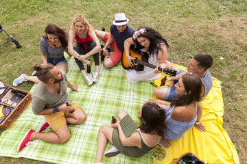 freunde sitzen im kreis auf einer decke im garten und chillen bei gitarrenmusik und einem kühlen...