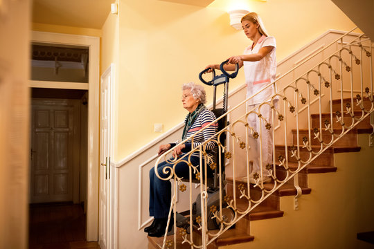 Nurse Using Machine For Climbing To The Stairs And Helps Old Mature Senior Disabled Woman