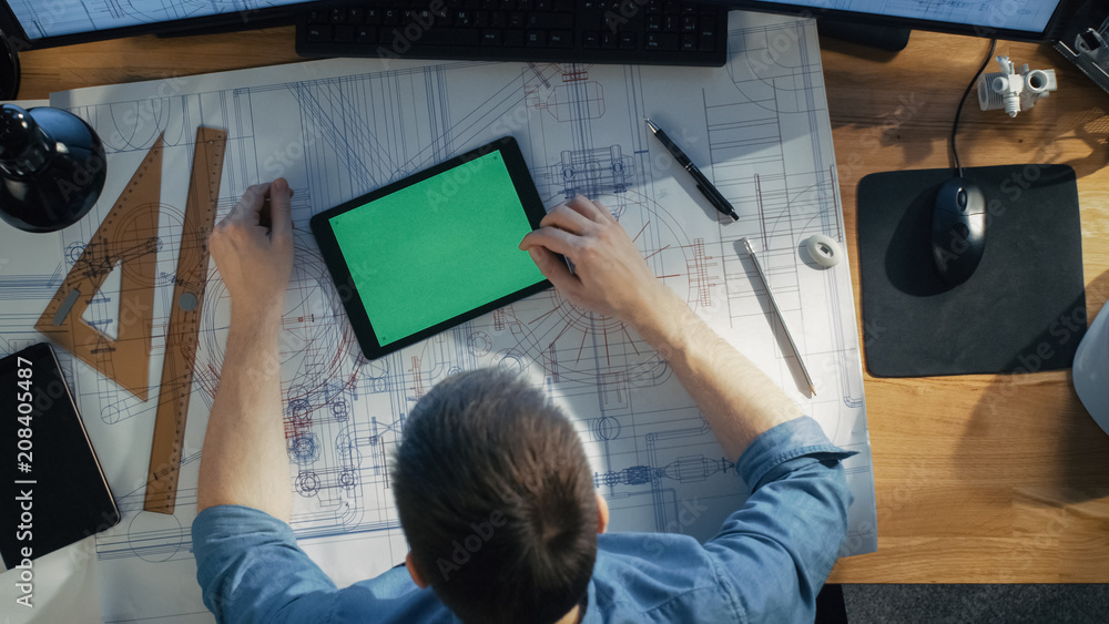 Poster top view of architectural engineer working with blueprints, uses tablet computer with green screen, 