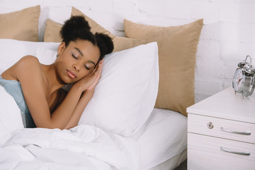 beautiful african american girl sleeping on bed with alarm clock near