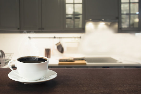 Cup of black coffee on wooden tabletop in blurred modern kitchen. Close up. Indoor.