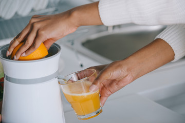 cropped shot of woman squeezing fresh orange juice at kitchen
