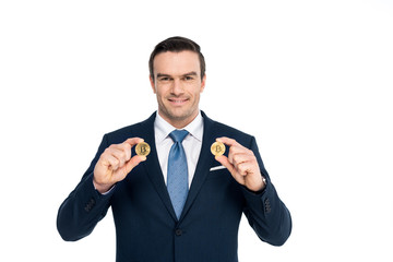 handsome middle aged businessman holding bitcoins and smiling at camera isolated on white