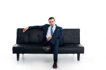 confident middle aged businessman sitting on couch and looking at camera on white