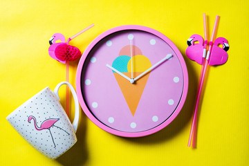 Creative summer top view with pink wall clock, coffee cup and flamingos on the yellow background. Flat lay