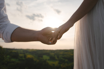 Close up two hands on sunset background. Groom holding bride hand. Wedding concept