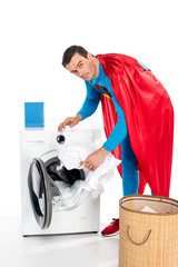 superman washing clothes in washing machine and looking at camera on white