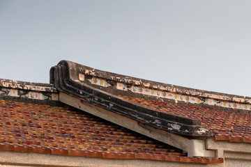 Traditional swallowtail style roof line found in historic villages in China and Taiwan. The building is brick with a decorative symbols on the roof line. There is a blue sky.