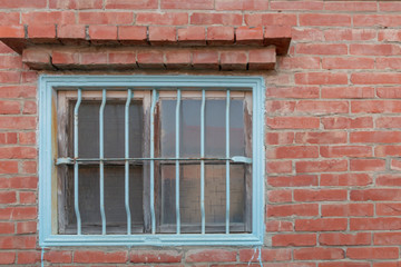 Fototapeta na wymiar Traditional Asian metal window security covering for a horizontal window. It is painted blue. The window is placed in a brick building. There is a brick overhang above the window.