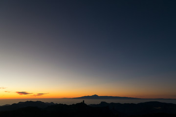 Silhouettes of Teide and Roque Nublo. Both islands separated by a sea of ​​clouds. and a sunset