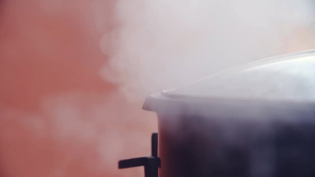 Steam leaving the cooking pot all around the cover in slow motion 4K. Long shot of the edge of cooking pot in focus with hot steam leaving from under the cover. Orange background.