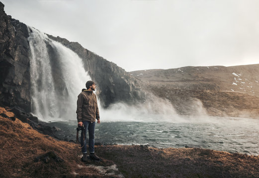 Young man standing near waterfall with camera