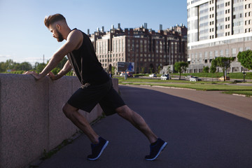 Sideways outdoor picture of handsome young male jogger with stubble and muscular athletic body...
