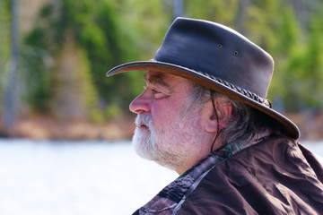 A peaceful caucasian man, 50's, wearing a white beard, a leather hat Australian style and a...