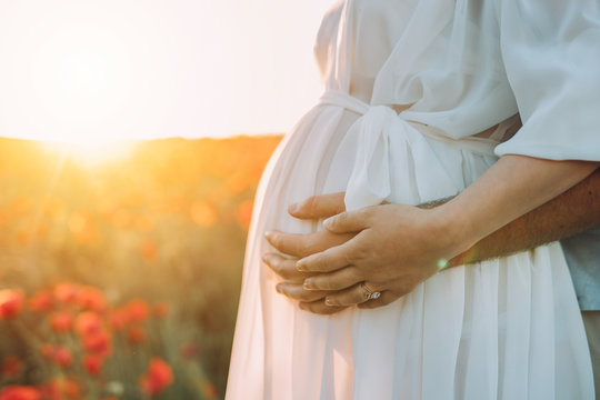Future parents embrace a pregnant tummy.Against the backdrop is a very beautiful summer sunset.