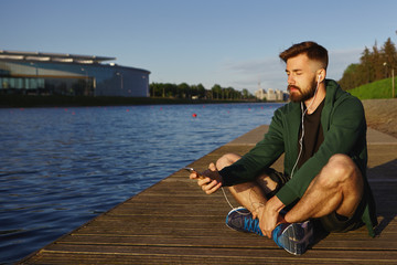 Outdoor shot of handsome unshaven young guy with stubble spending peaceful summer morning alone by...