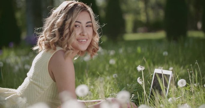 beautiful Asian girl surrounded by dandelions in the Park on a Sunny day with laptop, having fun slow motion
