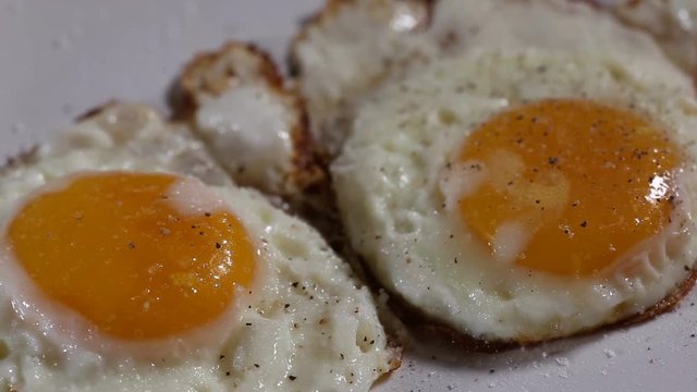 Spreading Ground Black Pepper Over Two Fried Eggs On The White Plate