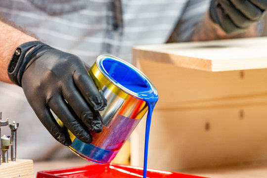 Male hand in gloves pouring paint into tray, closeup