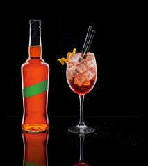 A liquor bottle and a cup of Spritz. Cold cocktail typical at Italian aperitivo or apericena on black background.