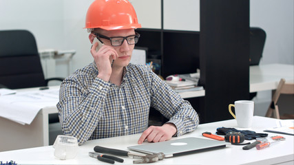 Young architect in helmet having important phone call