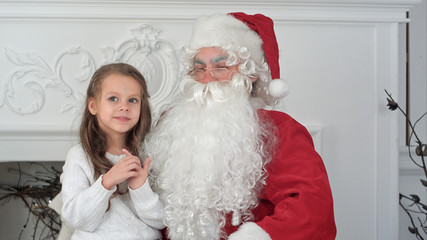 Obraz premium Santa Claus sitting in a chair with a little girl dreaming about her Christmas presents
