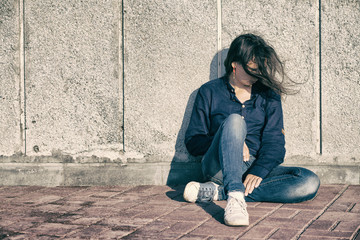 A teenage girl with depression sits alone on a concrete wall background