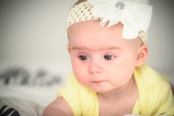 Cute infant girl on bed on belly lifting head little sad with tears in her eyes