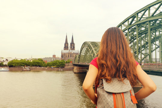 Traveling in Europe. Young female traveler with long hair and backpack enjoying the view of Cologne Cathedral and Bridge, Germany.